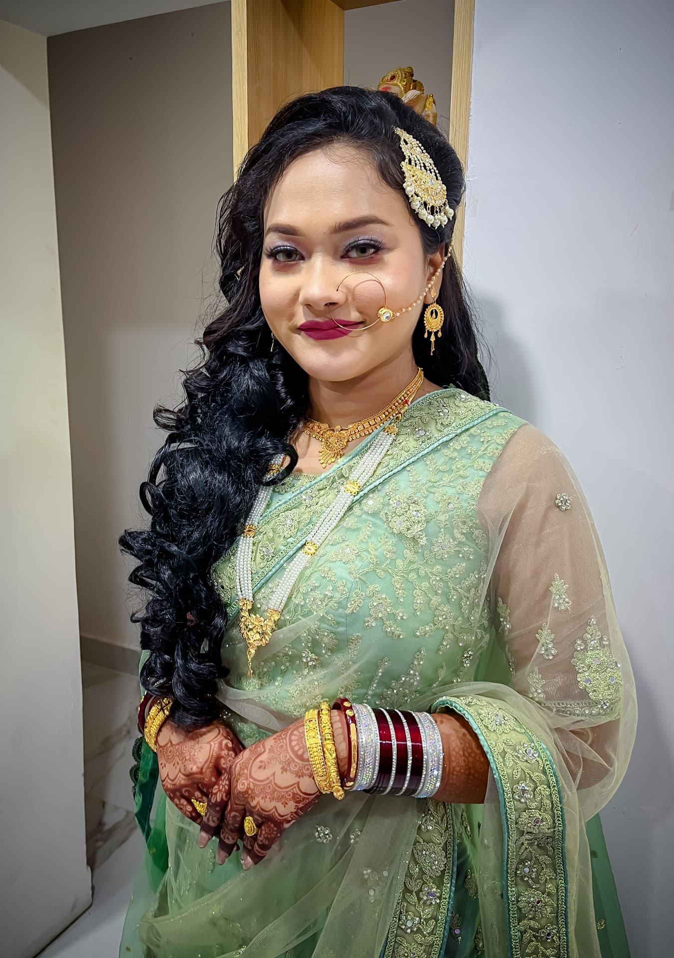 Bride in a mint green embroidered net sari with soft curls, pearl jewellery and henna-adorned hands
