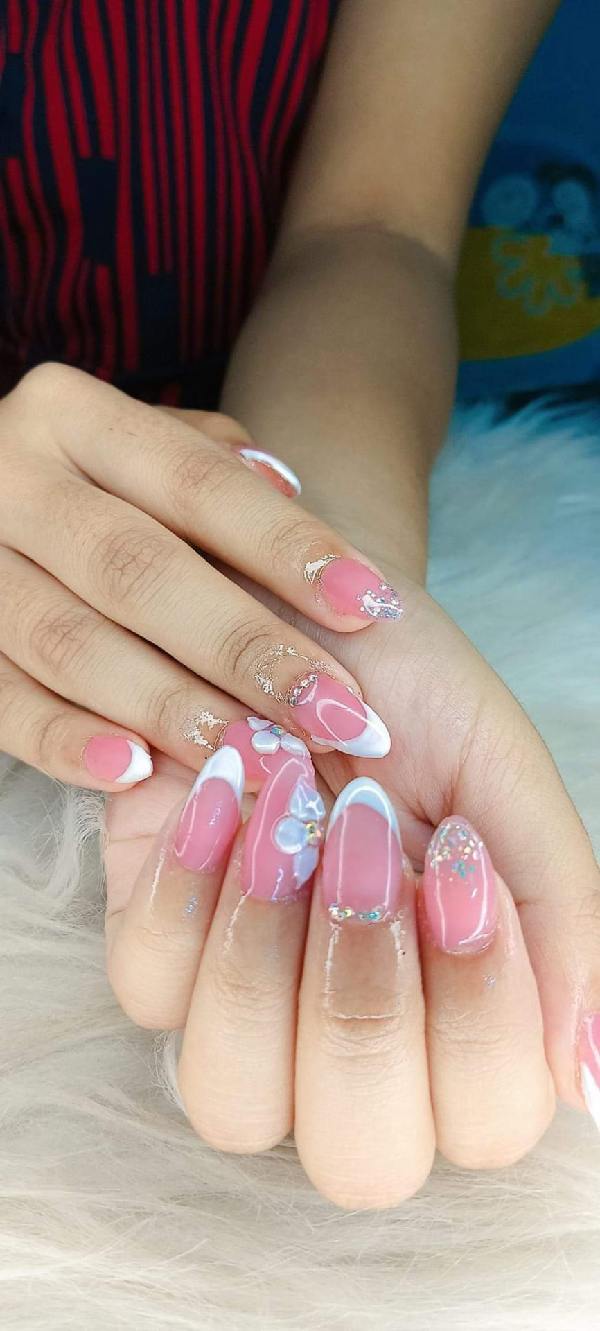 Hands with elegant pink French tip nail art featuring 3D floral accents and sparkling glitter details