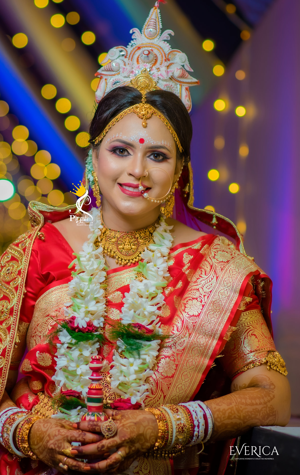 Smiling bride in a red benarasi wearing a handcrafted shola crown and jasmine garland